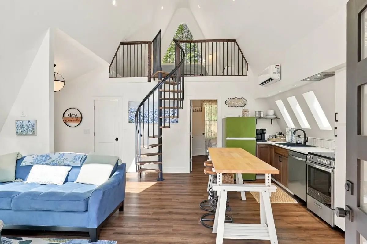 Open living room and kitchen under the A-frame peak, with a blue sofa, a butcher-block table, a green fridge and a spiral staircase up to the loft