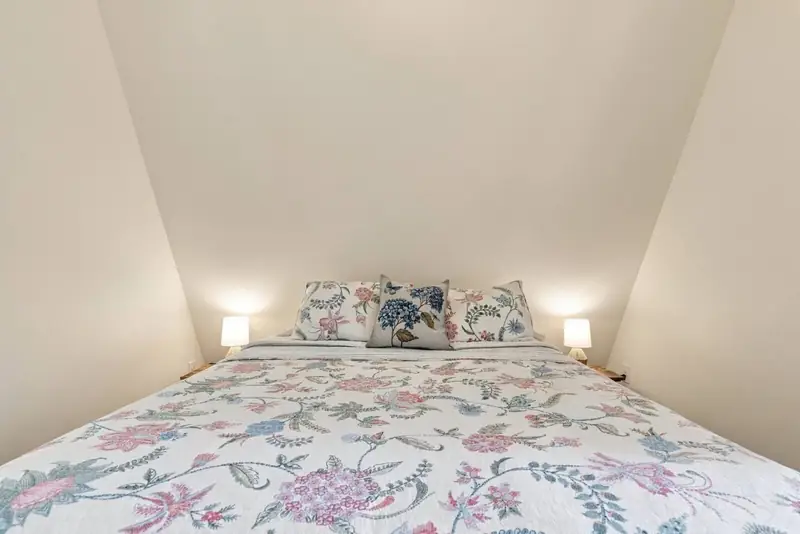 Queen bed with a floral quilt in the loft, under the sloped walls of the A-frame